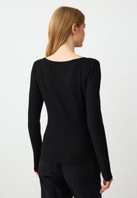 Langärmliges schwarzes Oberteil mit gerippter Textur und weitem Ausschnitt, das eine figurbetonte Silhouette und glatte Nähte ohne sichtbare Beschläge aufweist.