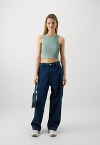 Mint zeleni rebrasti crop top, labavi tamnoplavi traper cargo hlače širokih nogavica, upareni s bijelim tenisicama i malom traper torbom.
