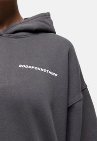 Sweat-shirt à capuche gris avec une texture douce et une coupe décontractée. Présente le texte blanc "GOODFORNOTHING" brodé à l'avant.
