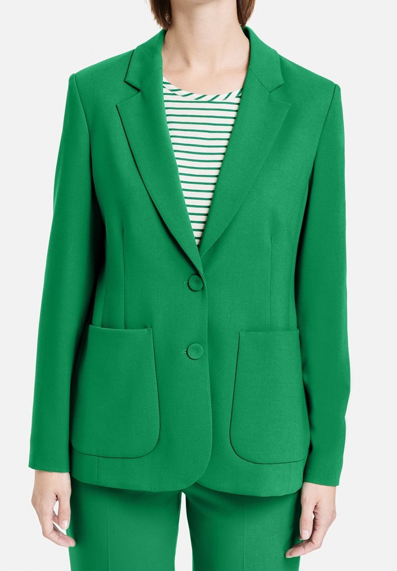 Blazer verde con dos bolsillos frontales, cierre de un botón, solapas con muesca y una textura suave. Combinado con una camisa de rayas verde y blanca.