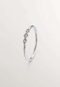 Anillo de plata con una banda delgada y tres pequeños diamantes redondos engastados en un grupo en la parte frontal. Acabado pulido, textura suave.