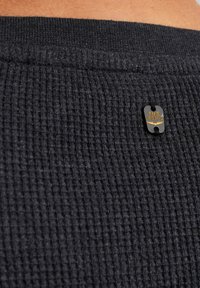 Schwarzer, strukturiert Stoff mit Rippmuster. Mit einem silbernen und goldenen PME Legend-Logoschild. Nahaufnahme, die sich auf das Material und die Details konzentriert.