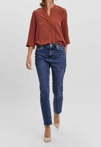 Rostfärgad blus med lång ärm och V-krage, löst sittande, kombinerad med mörkblå raka jeans och nude högklackade skor.
