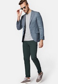 Niebieska kraciasta marynarka na szarej koszulce, ciemnozielone spodnie i szare sneakersy. Dodatki to srebrne okulary przeciwsłoneczne. Luźny, ale dopasowany wygląd.