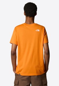 Orange bomulds t-shirt med korte ærmer og rund halsudskæring. Har et lille hvidt logo på den øverste del af ryggen. Glat tekstur, afslappet pasform.
