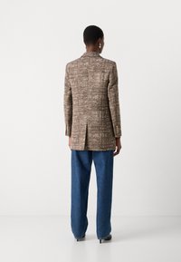 Brauner strukturierter Blazer mit einem Fischgrätmuster, einfach geschlitzt, mit goldenen Knöpfen, kombiniert mit blauen weiten Jeans.
