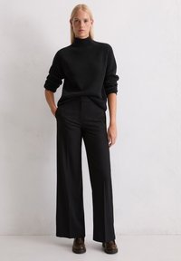 Must mustripsiga musta värvi kootud turtleneck-sviret, koos vabalt istuvate mustade pükstega ja tumpruunide nahkkingadega.