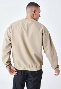 Beige bomberjack met een geribbelde boord en manchetten, gladde textuur en een relaxte pasvorm. Zichtbare stiksels en geen hardwaredetails.