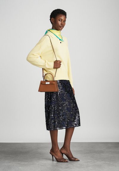 Suéter amarillo con cuello, combinado con una falda de lentejuelas azul marino. Bolso marrón, sandalias de tacón transparentes. Bufanda con acentos verdes alrededor del cuello.