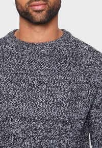 Pullover a maglia bianco e nero con un motivo testurizzato, dotato di un collo rotondo e polsini a coste. Vista ravvicinata che mette in evidenza i dettagli del tessuto.