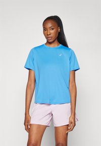 Camiseta atlética azul de tejido ligero con mangas cortas y escote redondo. Combinada con pantalones cortos rosa claro, ambos ajustados para el movimiento.