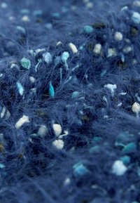 Teksturowana granatowa tkanina z drobnymi akcentami turkusu i bieli, o miękkim, puszystym wyglądzie oraz różnorodnej długości włókien.
