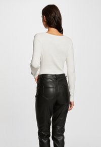 Haut à manches longues blanc côtelé associé à un pantalon en cuir noir taille haute avec poches arrière et coutures contrastées.