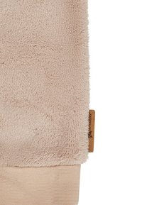 Nahaufnahme von beigem Fleece-Stoff mit einem gestrickten Bündchen und einem kleinen braunen Stoffetikett am Rand.