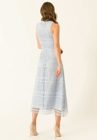 Světle modré krajkové šaty bez rukávů, s jemnými vzory a midi délkou. V kombinaci s tělovými vysokými podpatky.