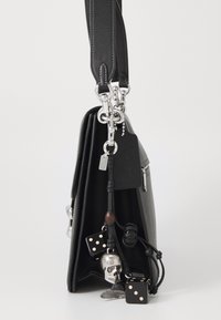 Borsa a mano in pelle nera con hardware argentato, dettagli in catena e charm decorativi tra cui un teschio e dadi. Presenta una superficie testurizzata.