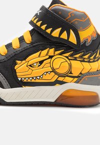 Baskets montantes noires avec motif de dragon jaune, accents orange, tissu texturé et col rembourré. Comprend une sangle Velcro et une semelle en caoutchouc.