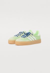 Lys grønne ruskinds sneakers med hvide accenter og tre hvide striber. Har blå og sølv snørebånd samt en sål i gummigummi.