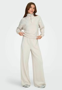 Lys beige zip-up sweatshirt med høj krave og lange ærmer, parret med vide matchende bukser. Blødt stof og afslappet pasform.