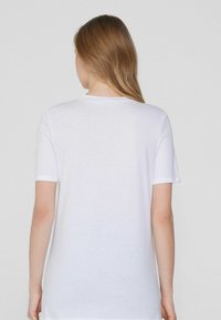 Camiseta blanca de manga corta con cuello redondo, hecha de material de algodón suave, que presenta un corte relajado y una textura suave.