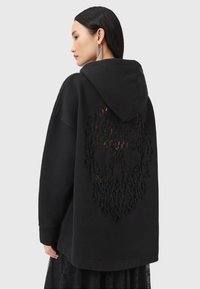 Felpa nera over-size con un design di teschio a taglio testurizzato sul retro, dotata di cappuccio e una silhouette comoda.