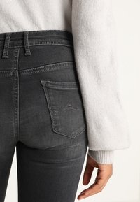 Dunkelgraue Jeans mit glatter Textur und leichtem Verblassen. Hat ein Fünf-Taschen-Design und genähte Details in der Nähe des Bundes.