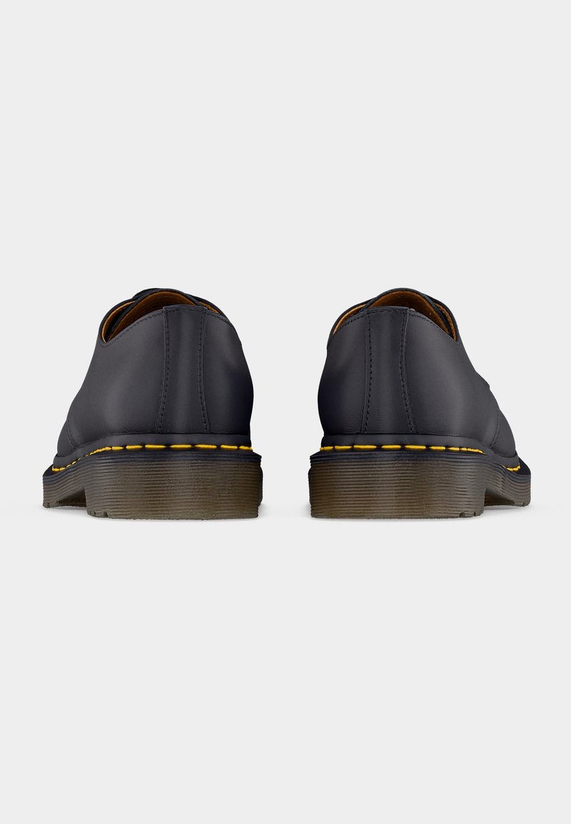 Scarpe in pelle nera con talloni arrotondati, cuciture gialle lungo la suola e suole in gomma impilate e strutturate. Design semplice, senza ornamenti.