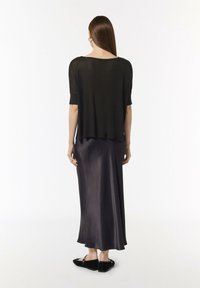 Czarny, lekki top z krótkim rękawem nałożony na ciemną satynową spódnicę. Spódnica ma gładką fakturę, zwiewny krój i sięga do połowy łydki.