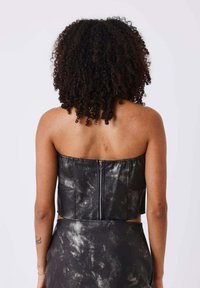 Black faux leather crop top with a zip back, featuring a smooth texture and subtle metallic accents. No shoulder straps, structured design.