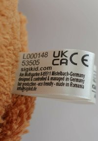 Soft orange plush fabric with a textured surface. Features a care label with black print, detailing manufacturing and eco-friendly status.