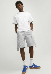T-shirt en coton blanc, shorts cargo gris avec poches, baskets bleues avec rayures blanches et chaussettes blanches mi-mollets. Tenue décontractée d'été.