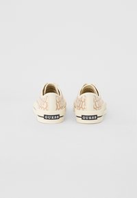 Vita sneakers med en texturerad mönster i ljus beige, med en svart "GUESS"-logotyp på hälen och en gummisula.