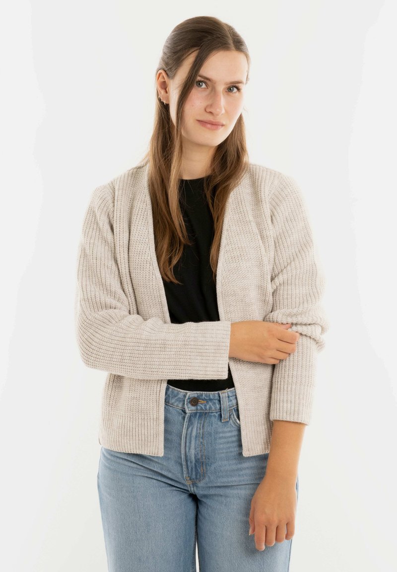 Lichtgrijze gebreide cardigan met ribbelstructuur en open voorkant, gecombineerd met een zwarte top en hoge taille blauwe jeans.