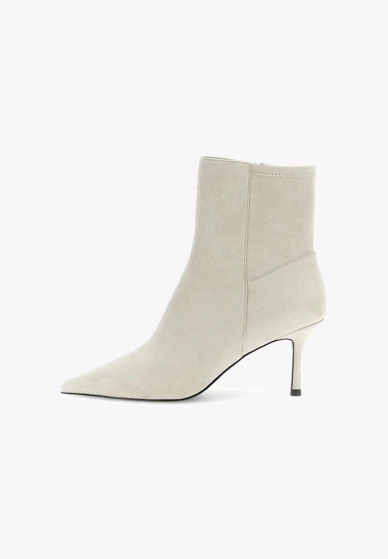 Béžová semišová kotníková bota s špičatou špičkou, úzkým podpatkem a bočním zipem na bílém pozadí.