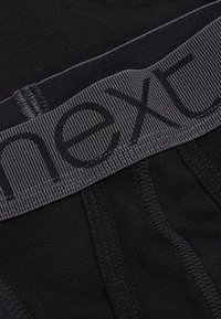 Schwarze Herrenunterwäsche mit einem grauen elastischen Bund, auf dem "next" in Schwarz eingeprägt ist. Glatte Textur und figurbetontes Design.
