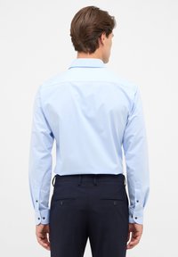  lichtblauwe langemouwen shirt met een standaard kraag, knoopmanchetten en een gladde textuur. Gecombineerd met donkere broek met knoopzakken.
