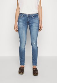 Pantalones vaqueros de corte ajustado en azul claro, confeccionados en denim, con una cintura de altura media, diseño de cinco bolsillos y un sutil desgastado en una pierna.