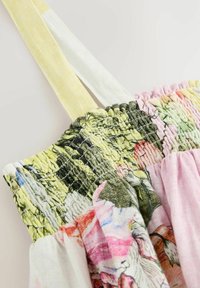 Kukkaprintillä varustettu mekko, jossa on rypytetty yläosa ja vihreän, vaaleanpunaisen ja keltaisen sävyjä. Ohutat, säädettävät olkaimet, joissa on tekstuurisia yksityiskohtia.