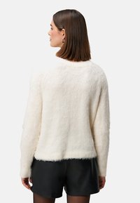 Cream fuzzy sweater with a relaxed fit, round neck, and ribbed hem. Paired with black shorts, showcasing soft texture and casual design.