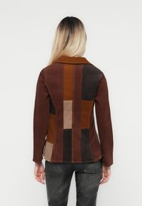 Bruine patchworkjas met een kraag, verweven stof, verschillende tinten bruin en een fitted ontwerp met zichtbare stikdetails.