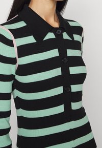 Maglione a righe nero e verde menta con colletto, dotato di chiusura a bottoni e texture a coste, accentuato da dettagli rosa sulle spalle.