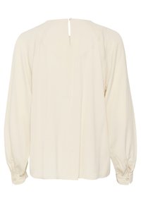 Blusa color crema con maniche lunghe, texture morbida, polsini abbottonati e chiusura a chiave sul retro. Design semplice e fluido.