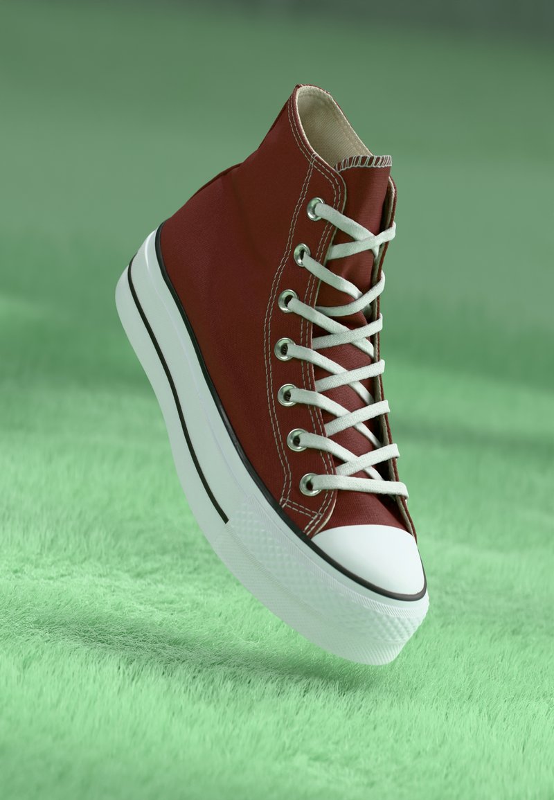 Punane kõrge säärega toss, mis on valmistatud kanvasest, valge kummist tallaga, musta aktsentjoonega ja valgete paeltega, asetatud rohelisele tekstuuriga pinnale.