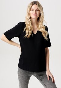 Svart kortärmad topp med V-ringning, gjord av mjukt material. Har en avslappnad passform och slät textur. Matchas med grå jeans.