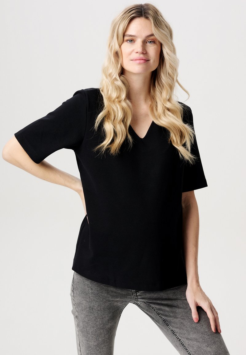 Svart kortärmad topp med V-ringning, gjord av mjukt material. Har en avslappnad passform och slät textur. Matchas med grå jeans.