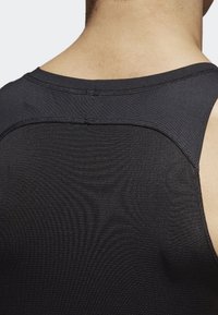 Débardeur de sport noir en tissu texturé, coupe ajustée et coutures lisses. Aucun motif ou élément métallique visible.