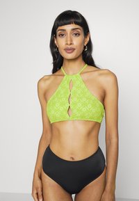 Zelený bikiny top s vzorem a detaily ve tvaru klíčové dírky, zavazovaný tenkými ramínky, spárovaný s černými bikinovými kalhotkami s vysokým pasem.