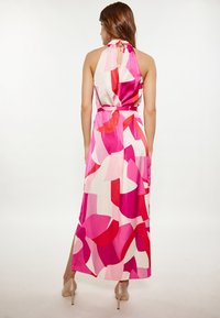 Rochie maxi dintr-un material foarte ușor, cu decolteu halter, un model abstract îndrăzneț în nuanțe de roz, roșu și alb, și un spate cu decupaj și închidere cu cârlig.