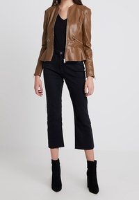 Giacca peplum in finta pelle marrone con tasche con zip, abbinata a jeans neri a vita alta e stivaletti neri. Design semplice e moderno.