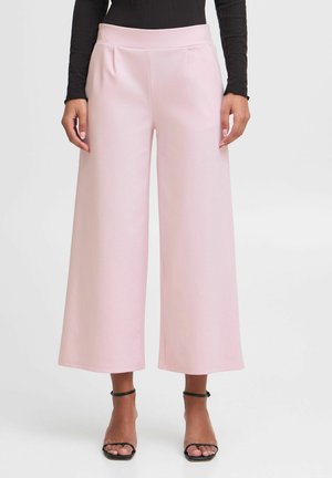 Pink wide-leg trousers with a smooth texture, featuring a high waistband and front pleats, paired with black strappy heels.